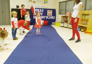 Lila ubrana na biało czerwono pozuje podczas "Pokazu mody patriotycznej" na granatowym dywanie.